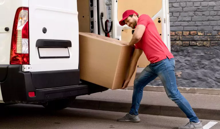 young professional trying to load a heavy cardboard into a van